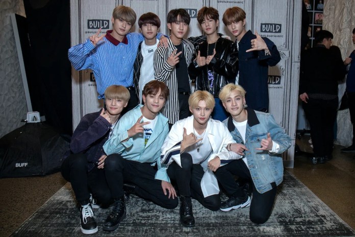 A group of nine young men posing together for a photo, smiling and making hand gestures, in a stylish indoor setting with a backdrop indicating a build series event.