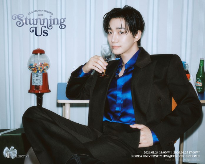 A stylish individual sitting comfortably, dressed in a dark suit and blue shirt, holding a glass while seated next to a gumball machine and soft drink bottles. The background features vertical stripes and promotional text for a fan meeting event.