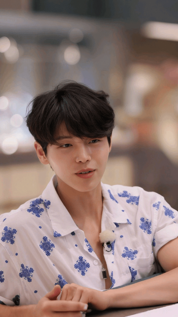 A person with dark hair wearing a white shirt with blue floral patterns, sitting at a table and looking attentively.