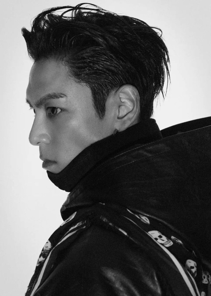 Profile shot of T.O.P with sleek, styled hair, wearing a black leather jacket with a decorative pattern. The image is in black and white.