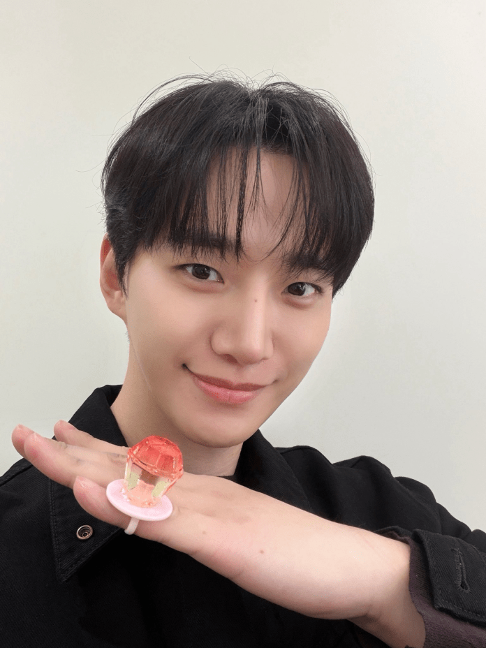 A smiling young person with dark hair is holding a colorful, transparent toy resembling a gem on their palm, against a neutral background.