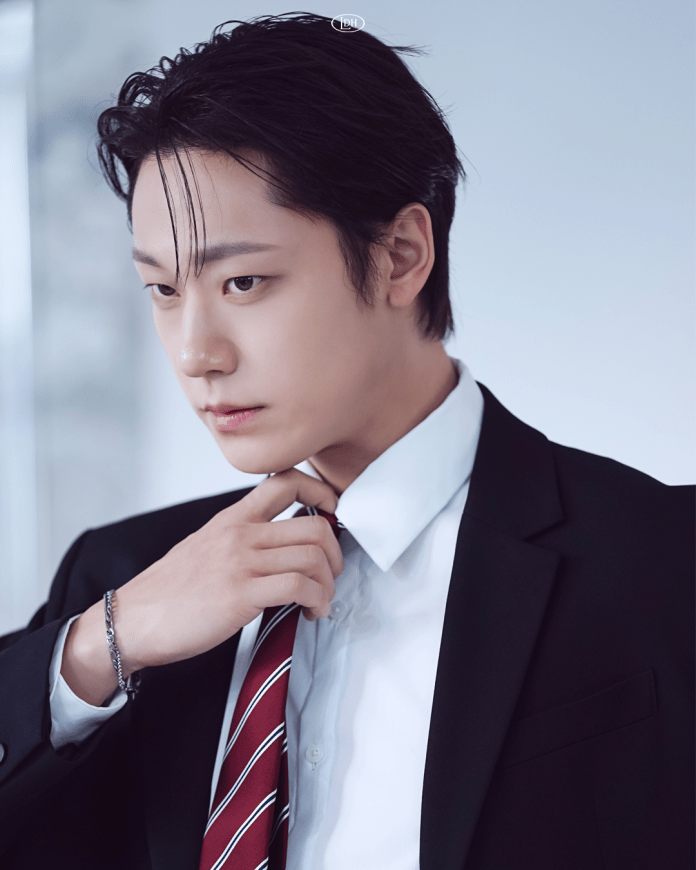 Lee Do hyun in a formal black suit and white shirt, adjusting his red-striped tie, with a thoughtful expression and styled dark hair.