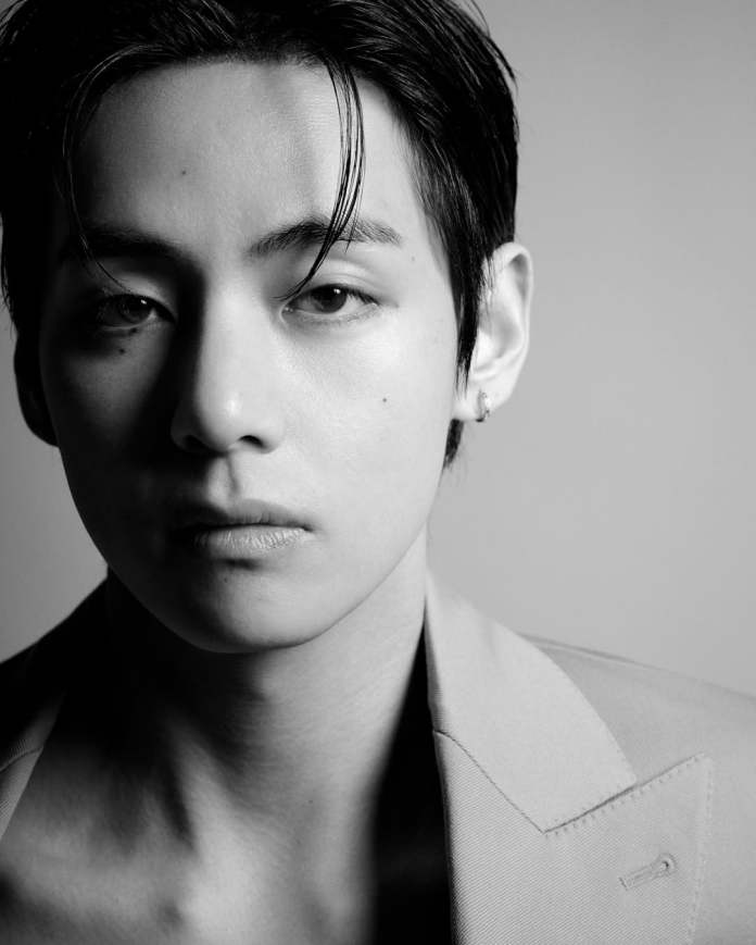 Close-up portrait of BTS V with sleek, dark hair, wearing a beige suit jacket against a neutral background.