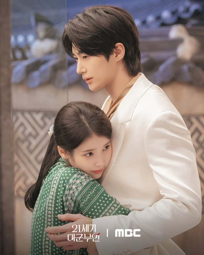 IU in a green traditional outfit embraces Byeon Woo-seok in a white suit, both appearing in a dramatic and tender moment.
