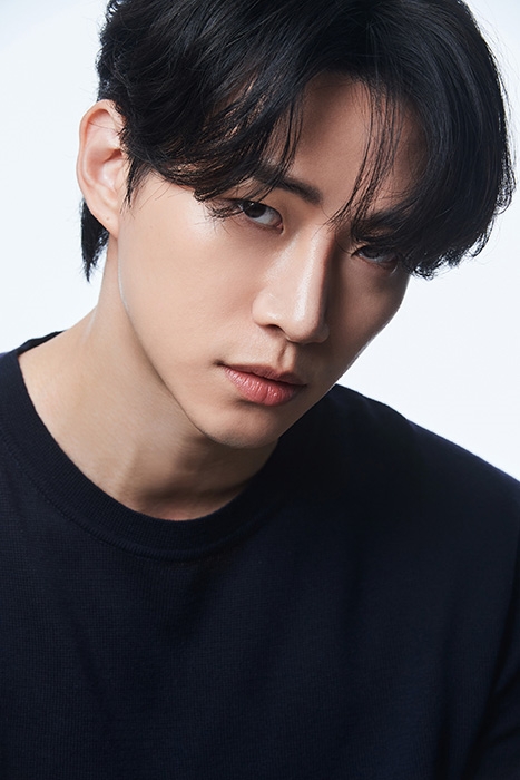 Close-up portrait of a Lee Junho with dark hair styled in a casual manner, wearing a black shirt against a light background.