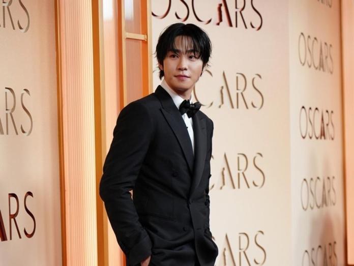 Ahn Hyo Seop dressed in a black tuxedo with a bow tie poses confidently at an Oscars event backdrop.