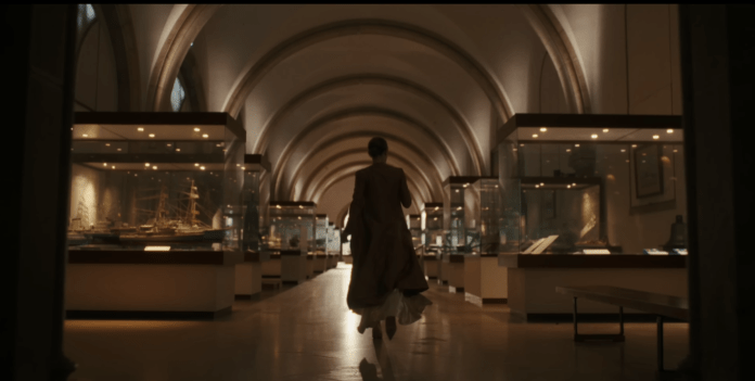 A person walking through a museum hall lined with display cases showcasing artifacts.