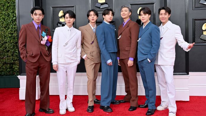 BTS pose together on the red carpet, wearing stylish suits of various colors at an awards event.