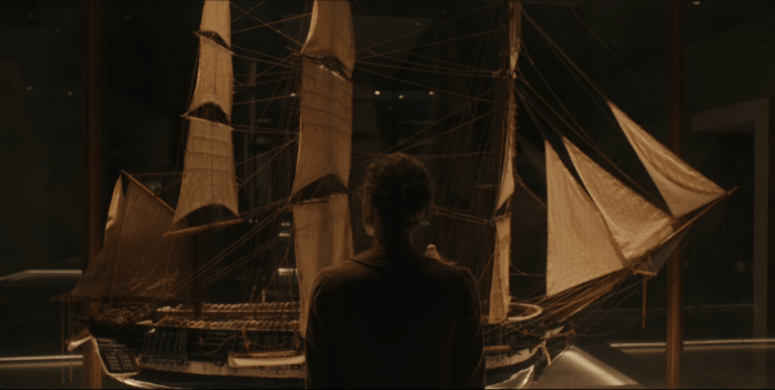 A person standing in front of a large model sailing ship displayed in a museum, with intricate details visible on the ship's sails and hull.