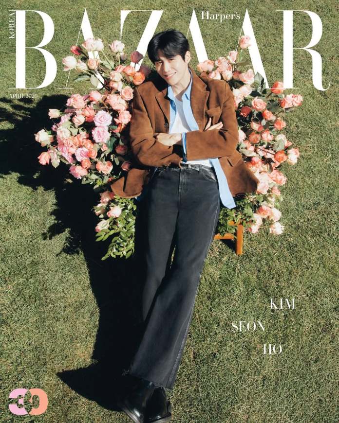 Kim Seon-ho surrounded by a bouquet of pink roses, featured on the cover of Harper's Bazaar Korea. He is wearing a brown jacket over a light blue shirt, with black jeans and black boots, smiling at the camera.