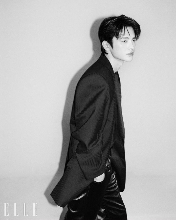 Seo In-guk in a stylish black blazer and pants, captured in a profile view against a soft, neutral background. The image is in black and white, emphasizing his facial features and sleek hairstyle.