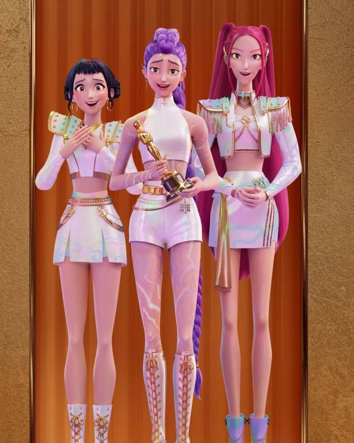 HUNTR/X standing together on a stage, celebrating with an award. The character in the middle holds an Oscar trophy, while the characters on either side display joyful expressions.