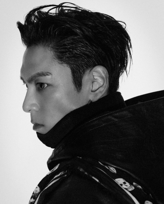 Profile view of T.O.P with slicked-back hair, wearing a dark jacket, set against a plain white background.