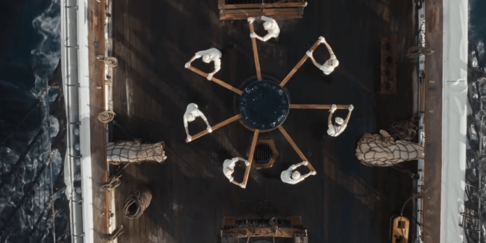 An overhead view of BTS on ship's deck performing synchronized rowing movements in unison around a central circular structure.
