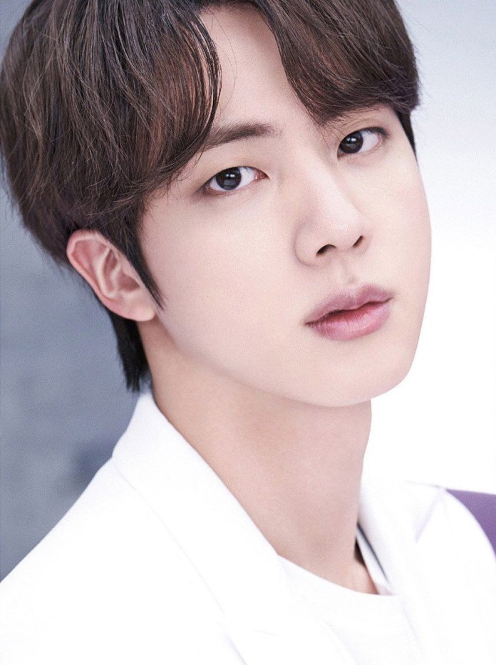 Close-up portrait of BTS Jin with dark hair, wearing a white jacket, looking directly at the camera.
