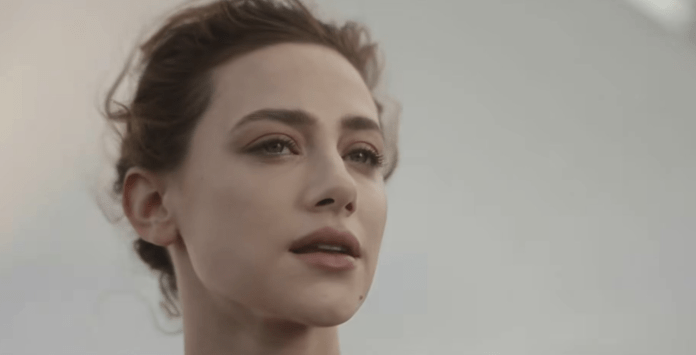 Close-up of a woman with wavy hair, looking thoughtfully into the distance with a neutral background.