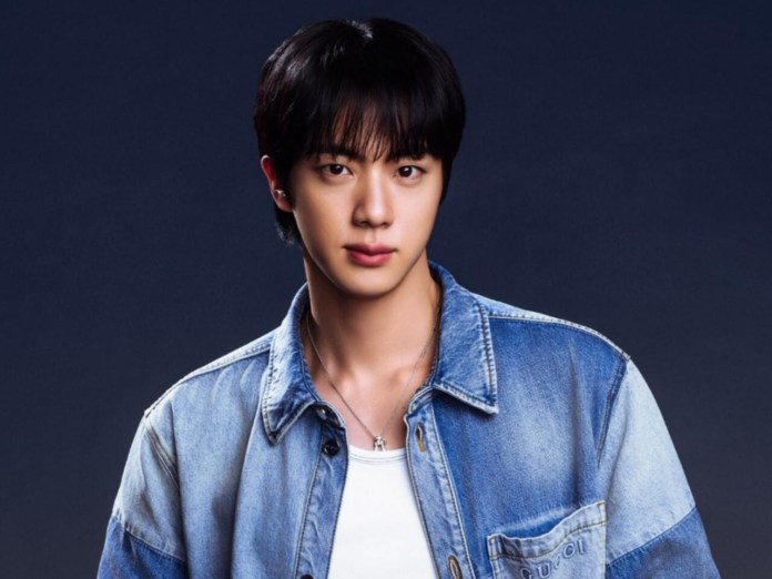 Portrait of a jin wearing a denim jacket over a white t-shirt, against a dark background.