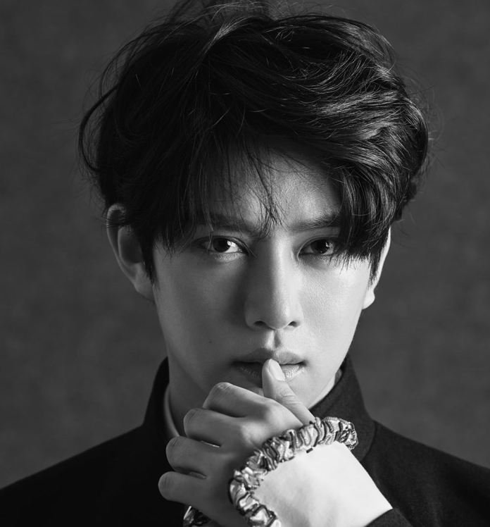 A close-up black and white portrait of Super Junior's Kim Heechul with tousled hair, expressing a thoughtful gaze while touching his lips with his fingers.