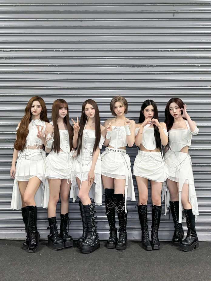 NMIXX posing together, wearing matching white outfits and black knee-high platform boots, standing in front of a metallic gray backdrop.