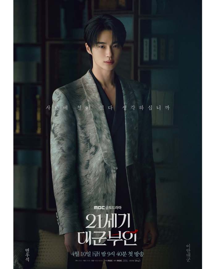 Byeon Woo-seok in a stylish patterned suit stands confidently, looking directly at the camera. The background features dark shelves with books, and text in Korean is featured prominently at the center of the image. The poster promotes the drama series Perfect Crown.