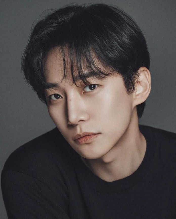 Close-up portrait of Lee Junho with dark hair, wearing a black shirt, against a neutral background, showcasing a thoughtful expression.