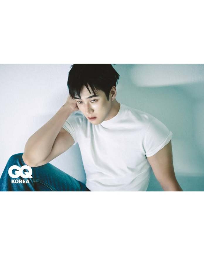 Ahn Bo-hyun in a white t-shirt sits against a light background, resting his head on his hand with a thoughtful expression. He is wearing blue jeans and has dark, styled hair.