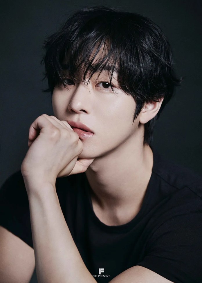 Ahn Hyo Seop with tousled black hair and a thoughtful expression, resting his chin on his hand, wearing a black shirt against a dark background.