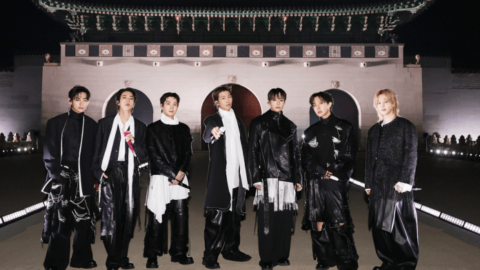 BTS members standing together in front of Gwanghwamun at night, wearing stylish, elaborate black and white outfits.