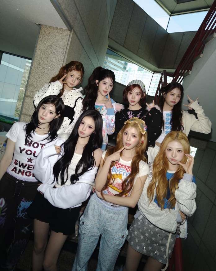 A group of nine young women posing together in a stairwell, wearing casual and stylish outfits. They are showing various expressions and gestures, with a mix of playful and serious poses.