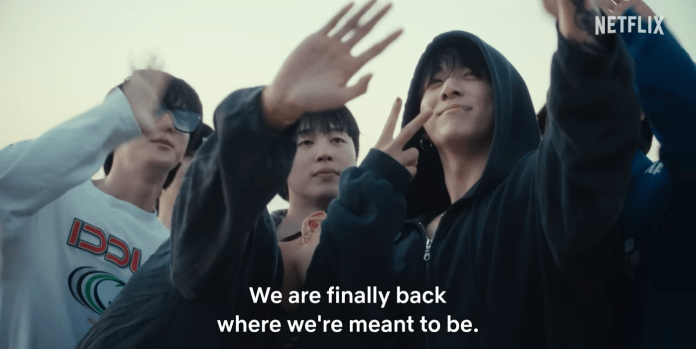 BTS members smiling and posing, with Jungkook making a peace sign. The scene conveys a sense of happiness and togetherness, with the phrase 'We are finally back where we're meant to be' displayed at the bottom.