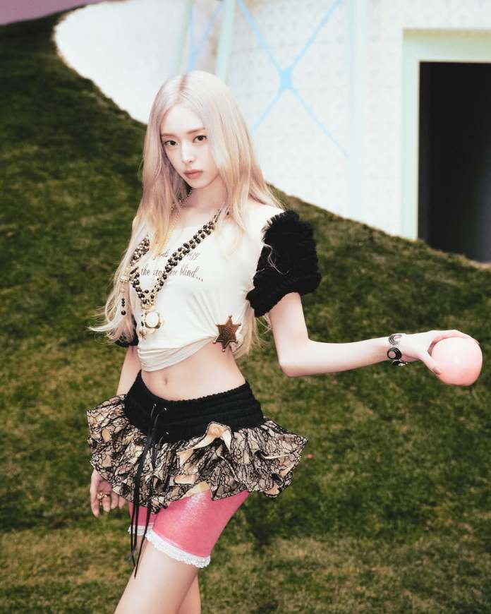 Yuna with long blonde hair poses in a playful outfit consisting of a cropped top and a ruffled skirt, holding a pink ball, with a green grass-like background.
