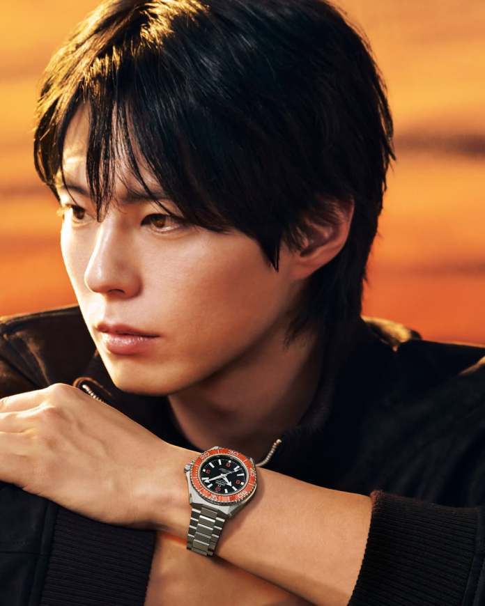 A close-up of Park Bo-gum looking thoughtfully to the side while wearing a stylish watch with a black face and orange accents on his wrist.