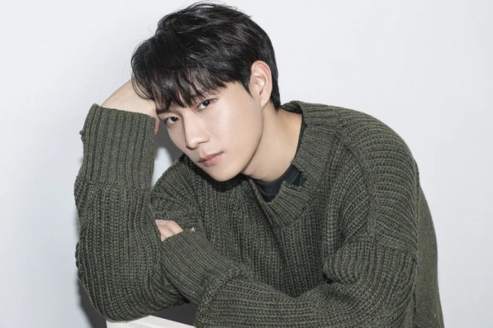 Kim Young Dae with dark hair and a serious expression, wearing a green knitted sweater, leaning on his arm against a light background.