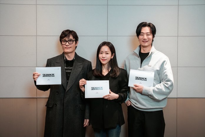 Three individuals holding signs that say '코리연즈' (Korean for 'Koryeon') in a studio setting.