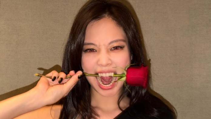 Jennie playfully biting a rose while smiling, with long dark hair and wearing a black top against a textured background.
