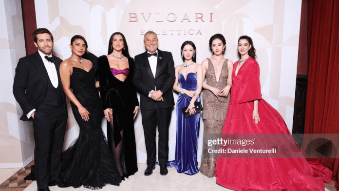 Kim Ji-won posing together at a Bvlgari event, featuring a man in a tuxedo and several women in stunning gowns of various colors.