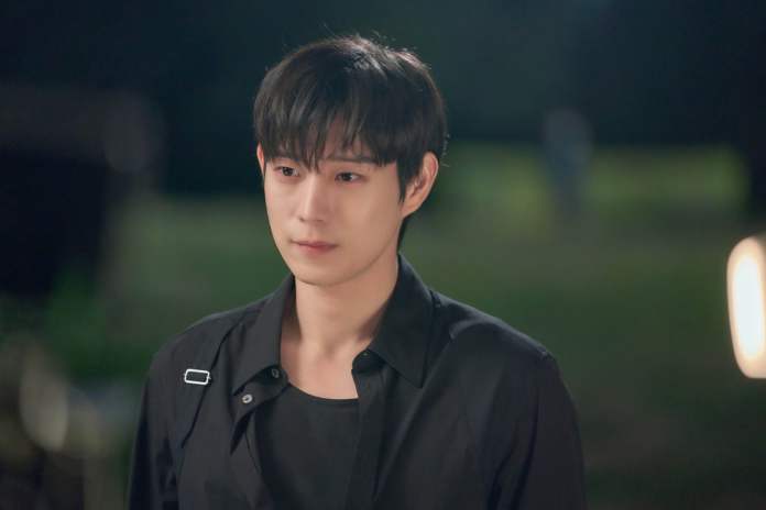 Kim Young Dae dark hair, wearing a black shirt, appears emotional in a dimly lit outdoor setting.