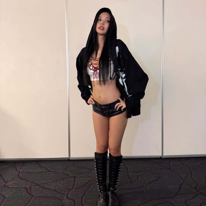 A person wearing a black oversized hoodie, a cropped white top with red detailing, and black shorts. They are standing confidently with hands on hips, featuring long black hair and knee-high boots.