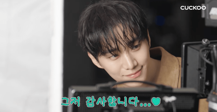 Lee Junho with tousled hair smiles while looking at a camera monitor, showcasing a warm and engaging expression.