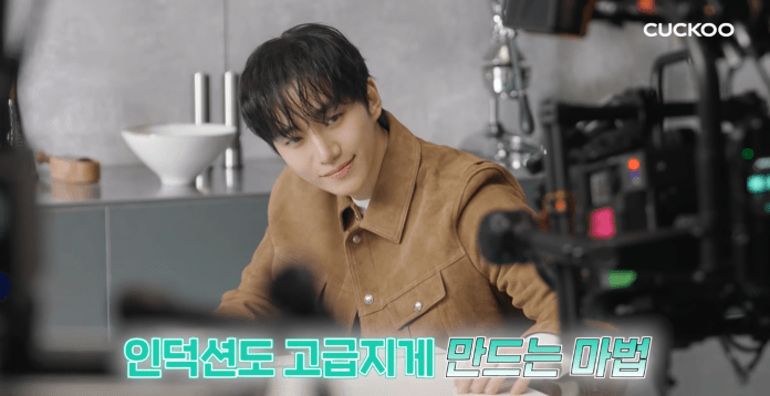 Lee Junho smiling while sitting at a table, with a camera setup in the foreground and a bowl in the background.