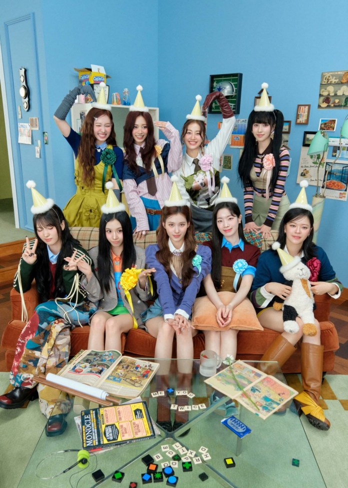 A group of nine young women wearing party hats posing happily in a brightly colored room, with a mix of casual and playful outfits, standing and sitting on a sofa surrounded by various decorations and games on a glass coffee table.