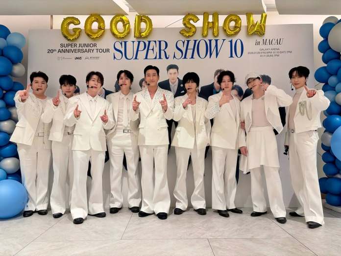 Super Junior members in white outfits pose in front of a promotional backdrop for Super Junior's 20th Anniversary Tour titled 'SUPER SHOW 10' in Macau, with balloons and a celebratory theme.