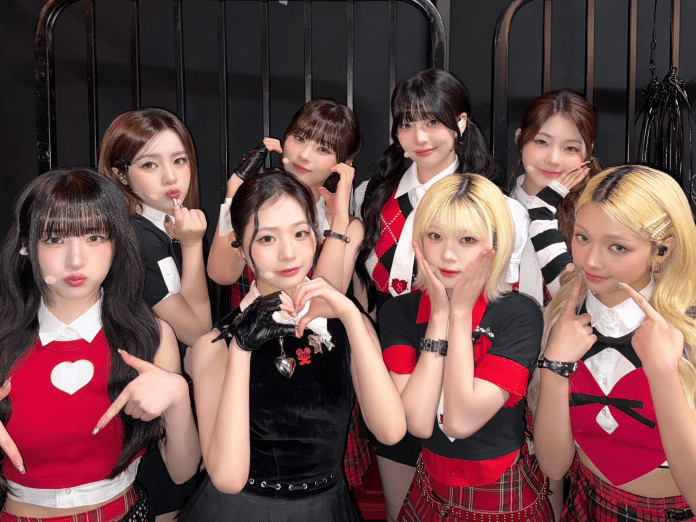 UNIS posing for a photo, wearing coordinated outfits with red and black colors, some showing playful hand signs. They are in a studio setting with a backdrop.