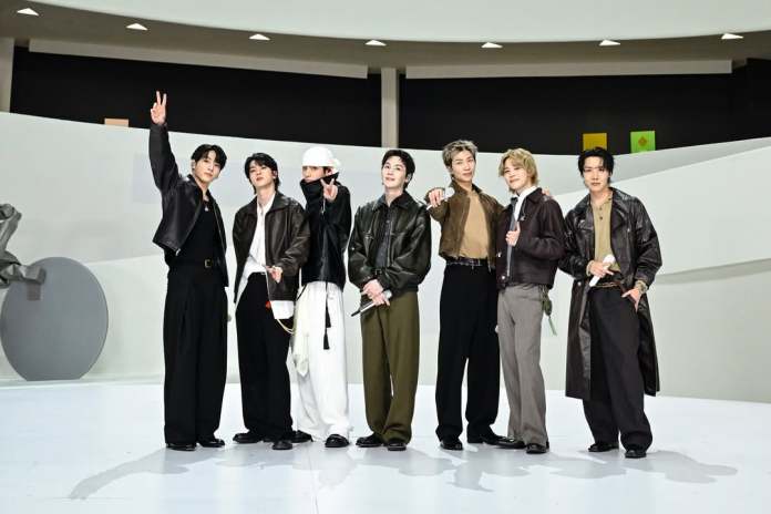 BTS members pose together in stylish outfits, showing camaraderie and a modern stage backdrop.