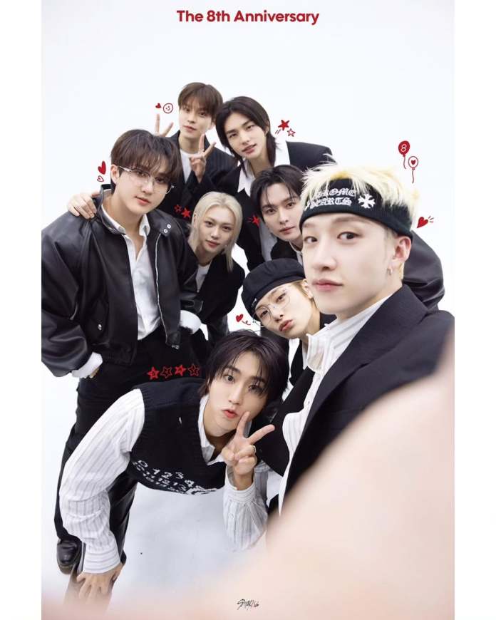 StrayKids posing together for a photo, celebrating their 8th anniversary. They are smiling and dressed in stylish outfits against a plain white background, with playful decorations like hearts and musical notes around them.
