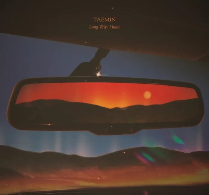 A car's rearview mirror reflecting a vibrant sunset over rolling hills, with the title 'TAEMIN Long Way Home' displayed at the top.