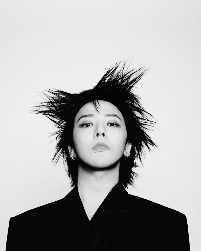 GD with spiky hair, wearing a black suit, gazing confidently at the camera.