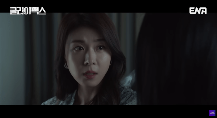 Ha Ji-won with long dark hair, looking intently with a serious expression, seated in a dimly lit room.