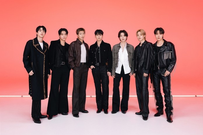 BTS posing together against a bright red background, wearing stylish and varied outfits, including coats, jackets, and trousers.