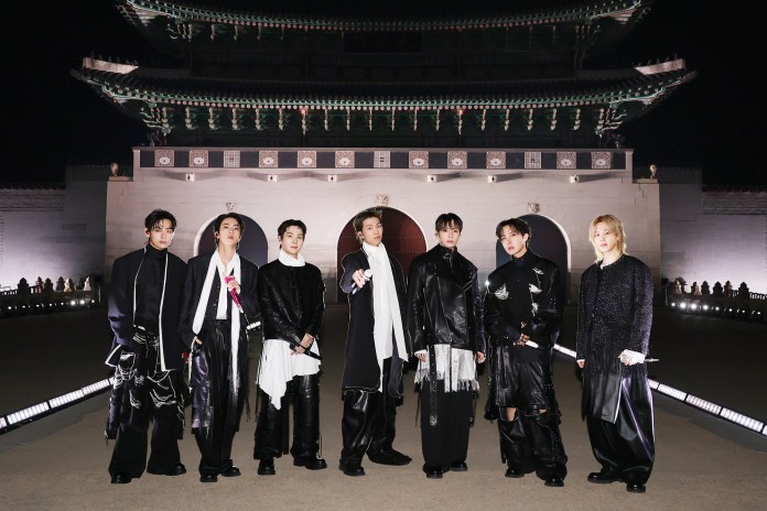 BTS stand in front of a historical building at night, wearing stylish black and white outfits.